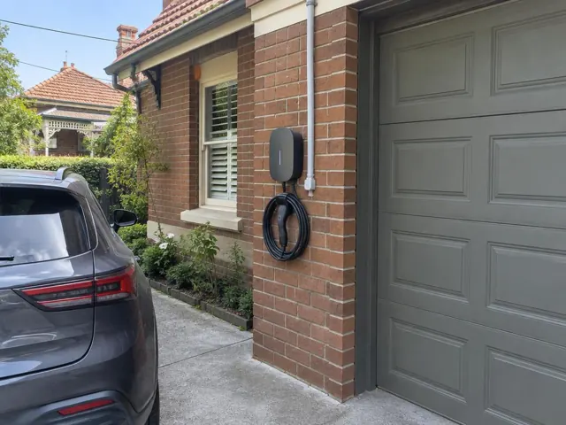 Wall-mounted EV charger and coiled cable on a brick exterior beside a garage door in Kensington